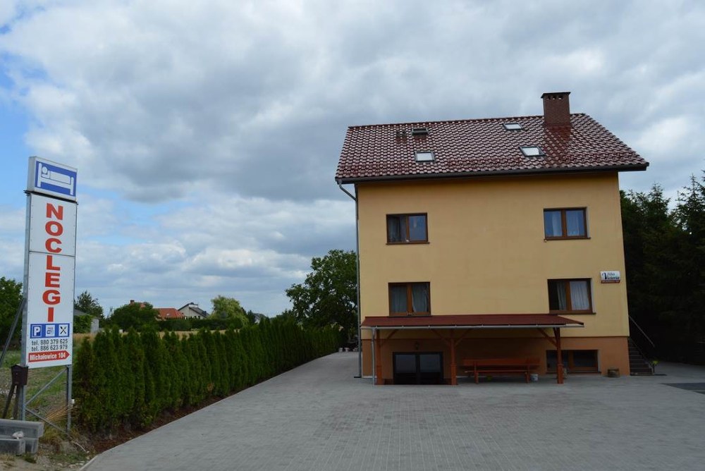 Budynek Villa Victoria w Michałowicach, żółta elewacja, wiata z ławami i tablica z napisem Noclegi